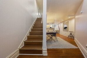 Una escalera conduce a un comedor con una mesa y sillas, un espejo en la pared y un taburete pequeño.