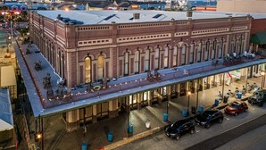 Suuri tiilestä rakennettu rakennus, jossa on tasakatto, katettu ulkoalue istumista varten ja pysäköintialue autoille.