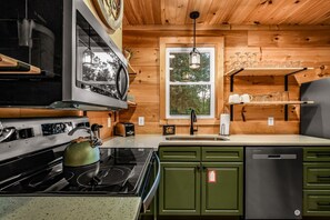 Une cuisine équipée d’une cuisinière, d’un four à micro-ondes et de meubles de rangement verts.