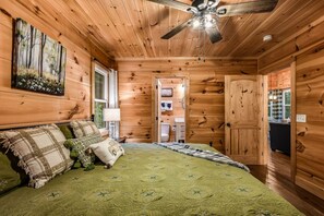 A wooden cabin bedroom with a bed, pillows, a ceiling fan, and a painting on the wall. - Shamrock Valley 1 Bedroom Cabin (Sevierville)