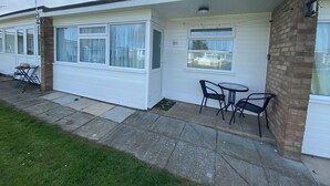 A white mobile home with a patio area, a small table, and two chairs. - Chalet 57 (Great Yarmouth)