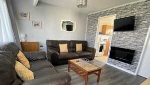 A living room with a sofa, a coffee table, a TV, and a stone wall. - Chalet 57 (Great Yarmouth)