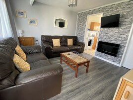 Uma sala de estar com um sofá, uma mesa de centro, uma televisão e uma parede de pedra.