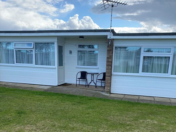 A mobile home with a patio area, two chairs, and a TV antenna. - Chalet 58 (Great Yarmouth)
