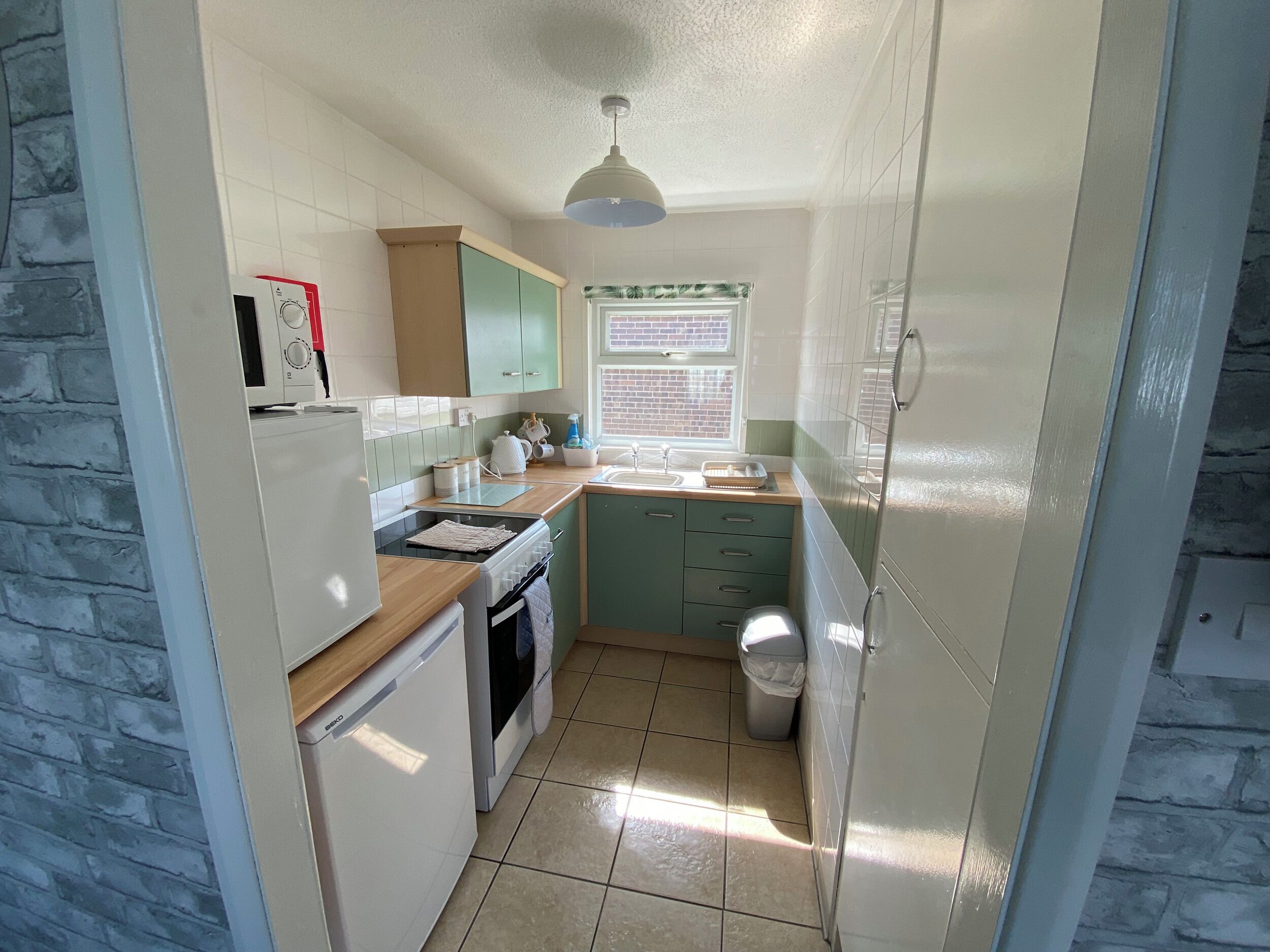 A compact kitchen with a refrigerator, stove, sink, and window.