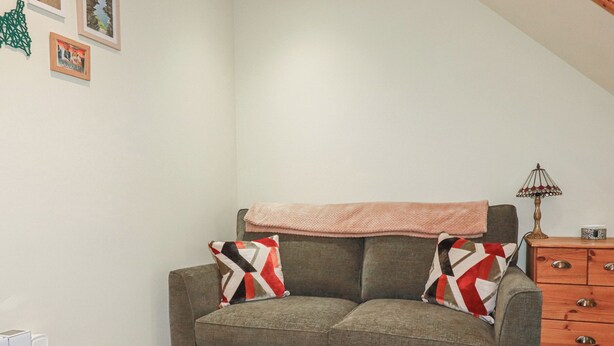 A grey sofa with patterned cushions, a wooden dresser, and a lamp. - Mini Mena (St Austell)