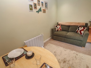 Ein Essbereich mit Tisch für zwei Personen, einem Heizkörper, einer grünen Couch mit gemusterten Kissen und gerahmten Bildern an der Wand.