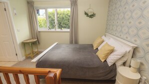 A bedroom with a bed, a bedside table, a window with curtains, a wall-mounted light, and a patterned wall. - Mini Mena (St Austell)