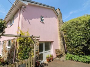 Ein rosafarbenes Gebäude mit einem Steinkamin, einer Holzpergola, einer Holzbank und einem Willkommensschild.