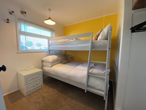 Quarto com beliche, uma mesa e uma luminária, além de uma janela.