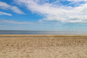 Uma praia com areal e turbinas eólicas ao longe.