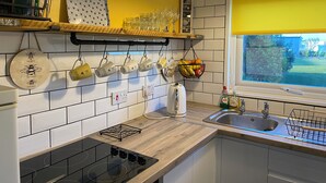 Una cucina con piastrelle bianche, un piano di lavoro in legno, un piano cottura integrato, una finestra con persiane gialle e tazze appese.