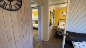 Una stanza con un letto, un tavolino, una sveglia e una porta che dà su un'altra stanza.