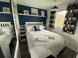 Quarto com cama, janela com cortinas, prateleira com quadros e uma planta.