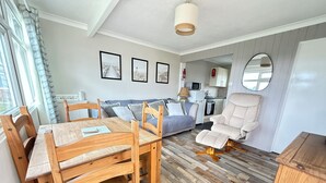 Una sala de estar acogedora con una mesa de comedor de madera, un sofá, un sillón reclinable y una cocina al fondo.