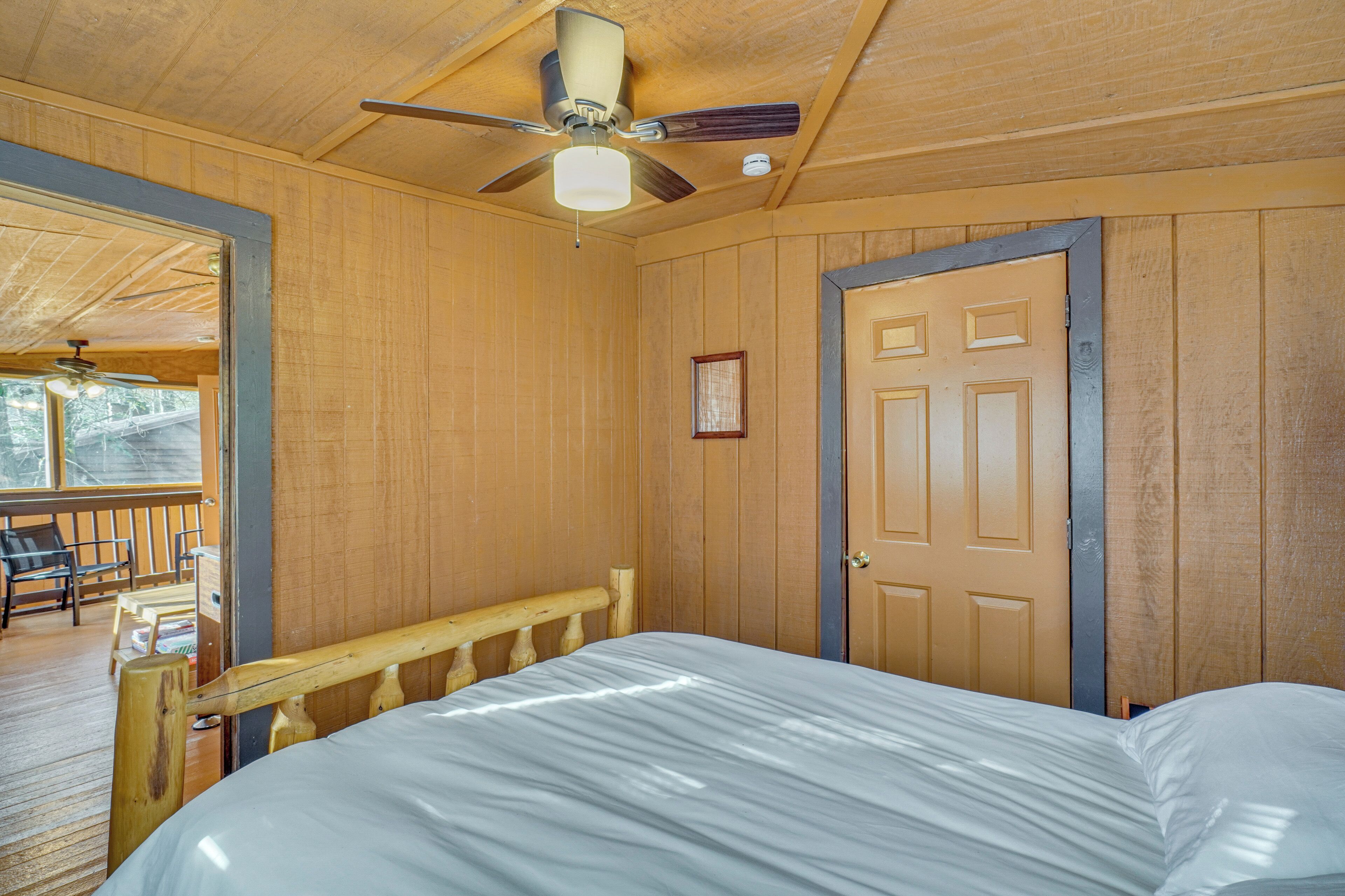 A wooden-paneled room with a bed, a ceiling fan, a door, and a window.