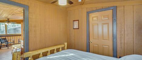 A wooden-paneled room with a bed, a ceiling fan, a door, and a window.