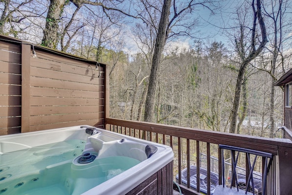 A hot tub on a wooden deck with a view of leafless trees and a clear sky.