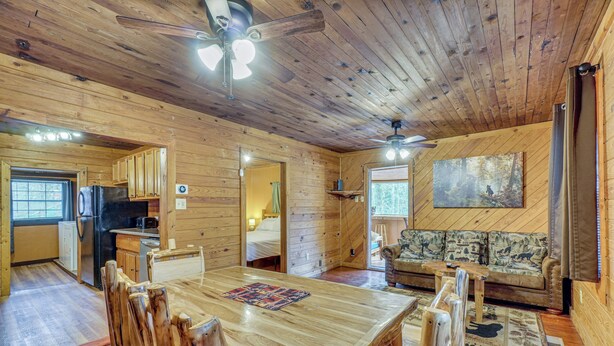 A wooden cabin interior with a dining table, chairs, a sofa, and a ceiling fan. - Private Hot Tub! Hillside Smokies Base Camp (Townsend)