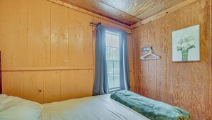 A wooden-paneled room with a bed, a window with curtains, a wall-mounted hanger, and a framed picture. - Private Hot Tub! Hillside Smokies Base Camp (Townsend)