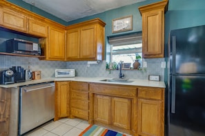 Una cocina con armarios de madera, microondas, refrigerador, lavavajillas y una ventana con una planta.