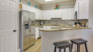 A kitchen with white cabinets, a stainless steel refrigerator, a granite countertop, and a small island with stools. - < 1 Mi to Beach: 30A Escape w/ Bikes + Pool Access (Santa Rosa Beach)