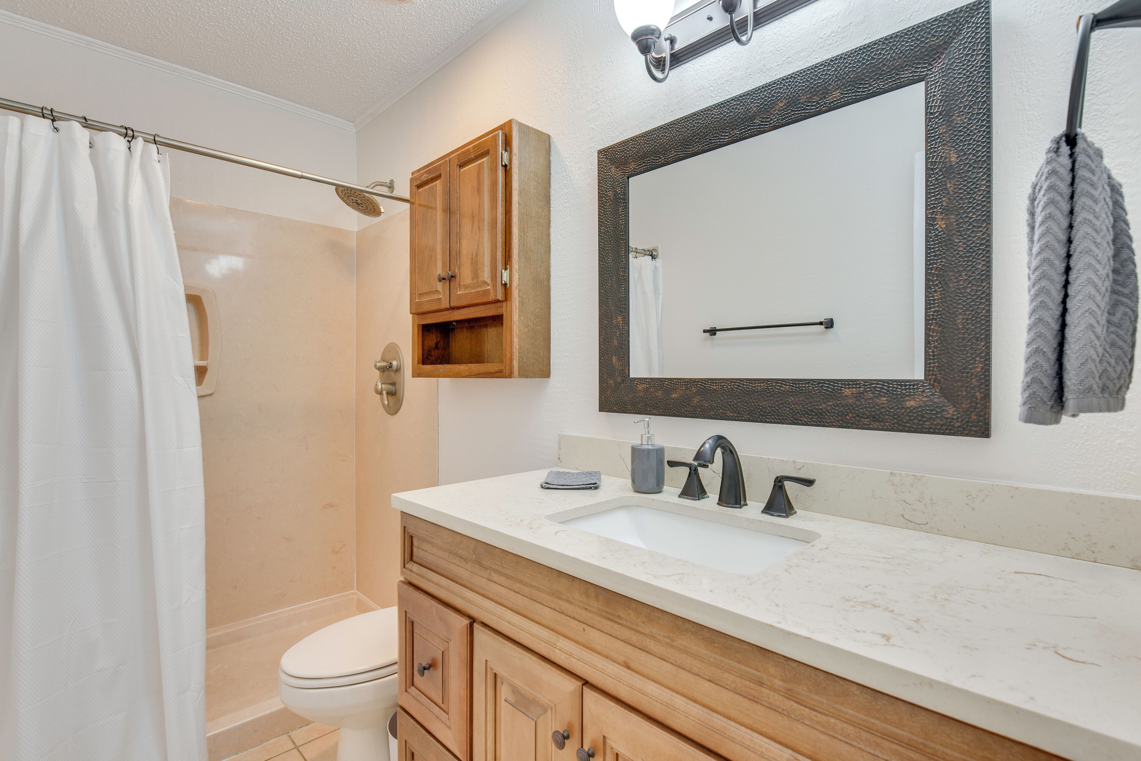 A bathroom with a shower, toilet, wooden vanity, and a large mirror.