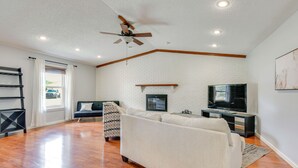 A living room with a white sofa, a TV, and a ceiling fan. - 4 Mi to Garniers Beach Park: Home w/ Private Pool! (Fort Walton Beach)