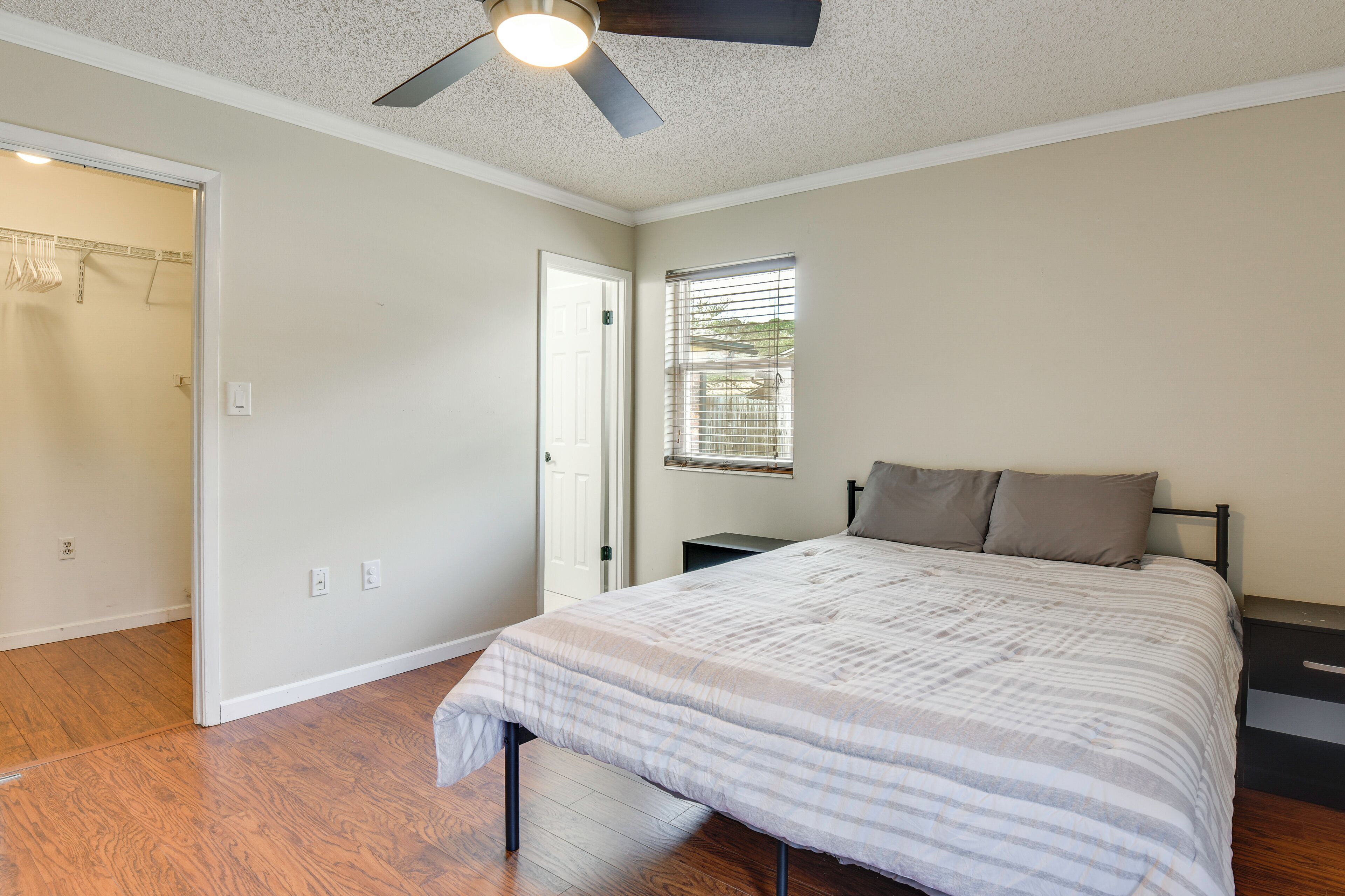 A bedroom with a bed, a ceiling fan, a window with blinds, and a door leading to a closet.
