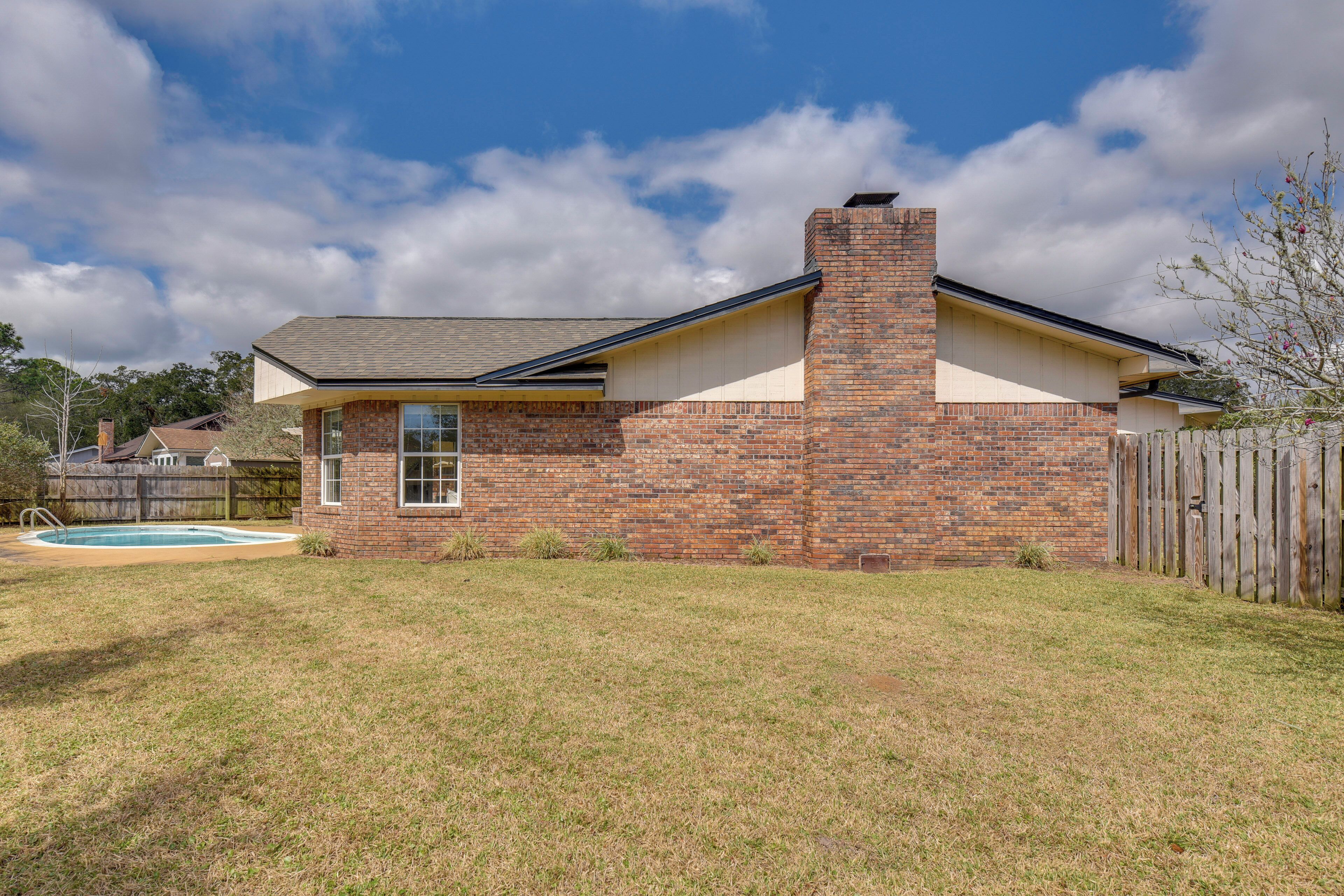 A single-story brick house with a chimney, a swimming pool, and a wooden fence.