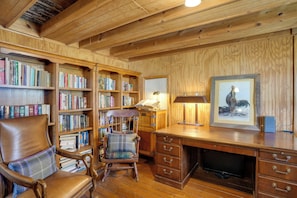 A wooden-paneled room with a leather chair, a desk, and bookshelves filled with books. - 'farm House at Fairview' Rustic Retreat in Amherst (Amherst)