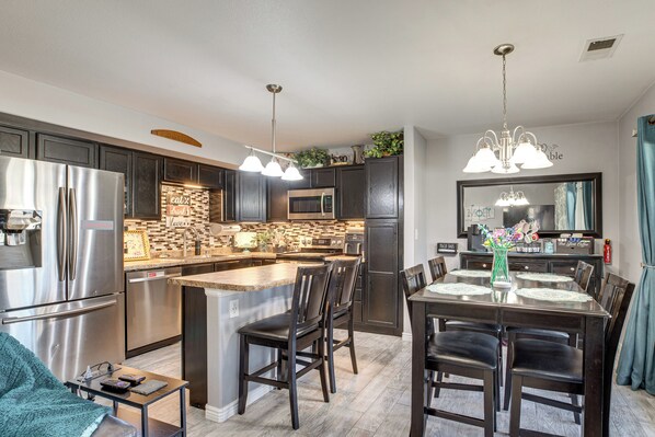 A modern kitchen with stainless steel appliances, a central island, dark wooden cabinets, and a dining area with a chandelier.