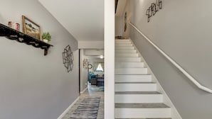 Ein Flur mit Treppe, einem Regal mit Dekoration und einem Teppich.