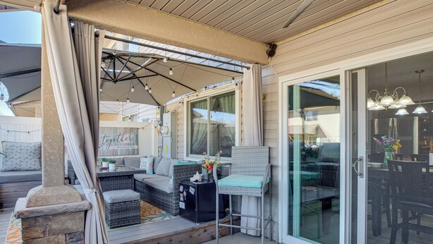 Ein überdachter Patio-Bereich mit Gartenmöbeln, einem Kamin aus Stein und einer Glastür, die zu einem Essbereich im Innenbereich führt.