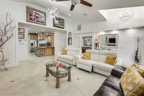 A spacious living room with a white sofa, a glass coffee table, and a dining area with bar stools. - Poolside Oasis: Group-friendly Getaway in Naples! (Naples)