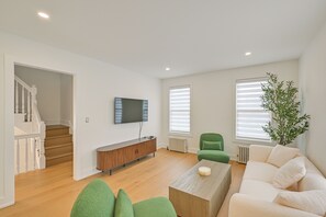 Un salon moderne avec un escalier, un téléviseur à écran plat, un fauteuil vert, un canapé blanc et une table basse en bois.
