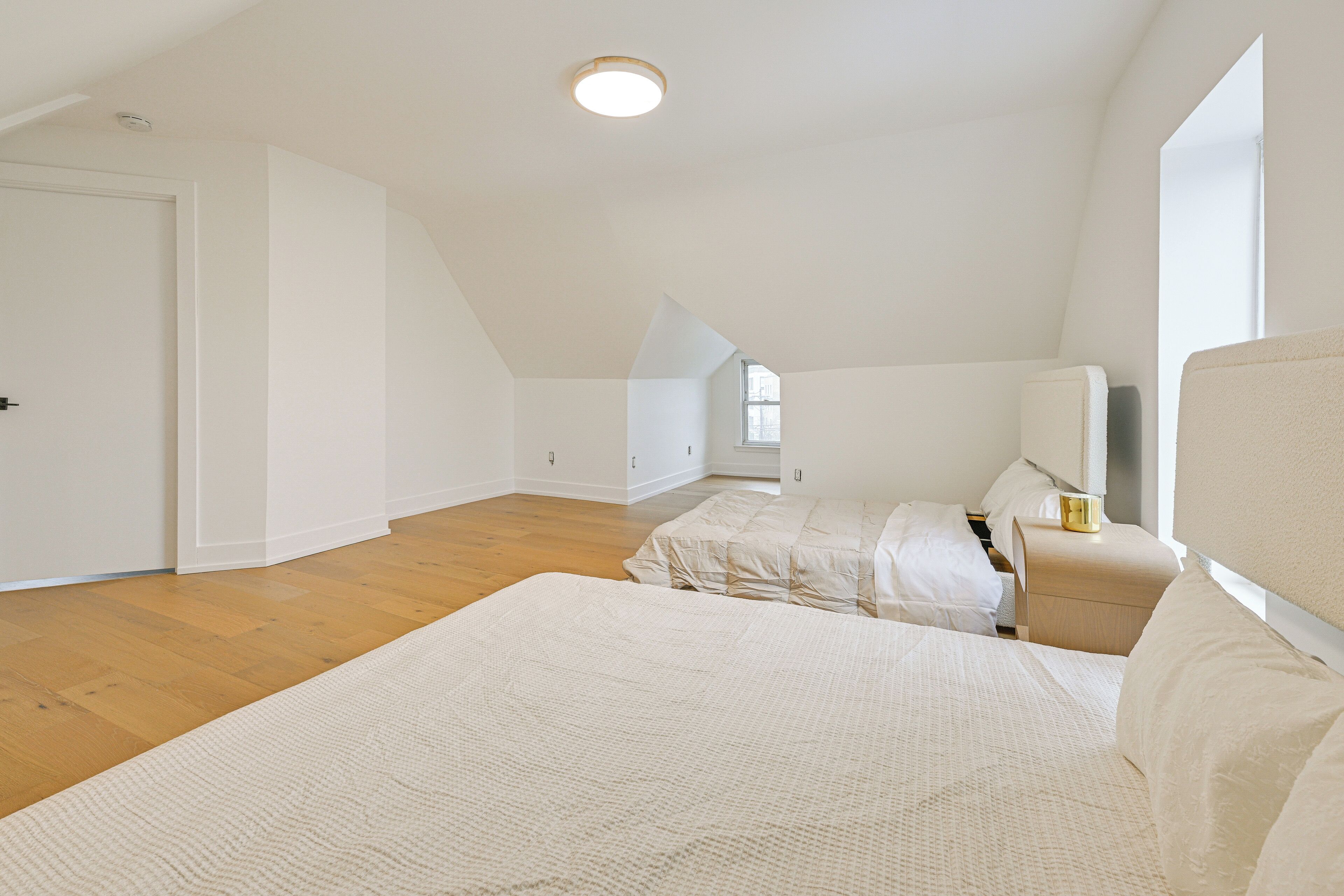 Een slaapkamer met schuine wand, een groot bed, een nachtkastje en een raam.