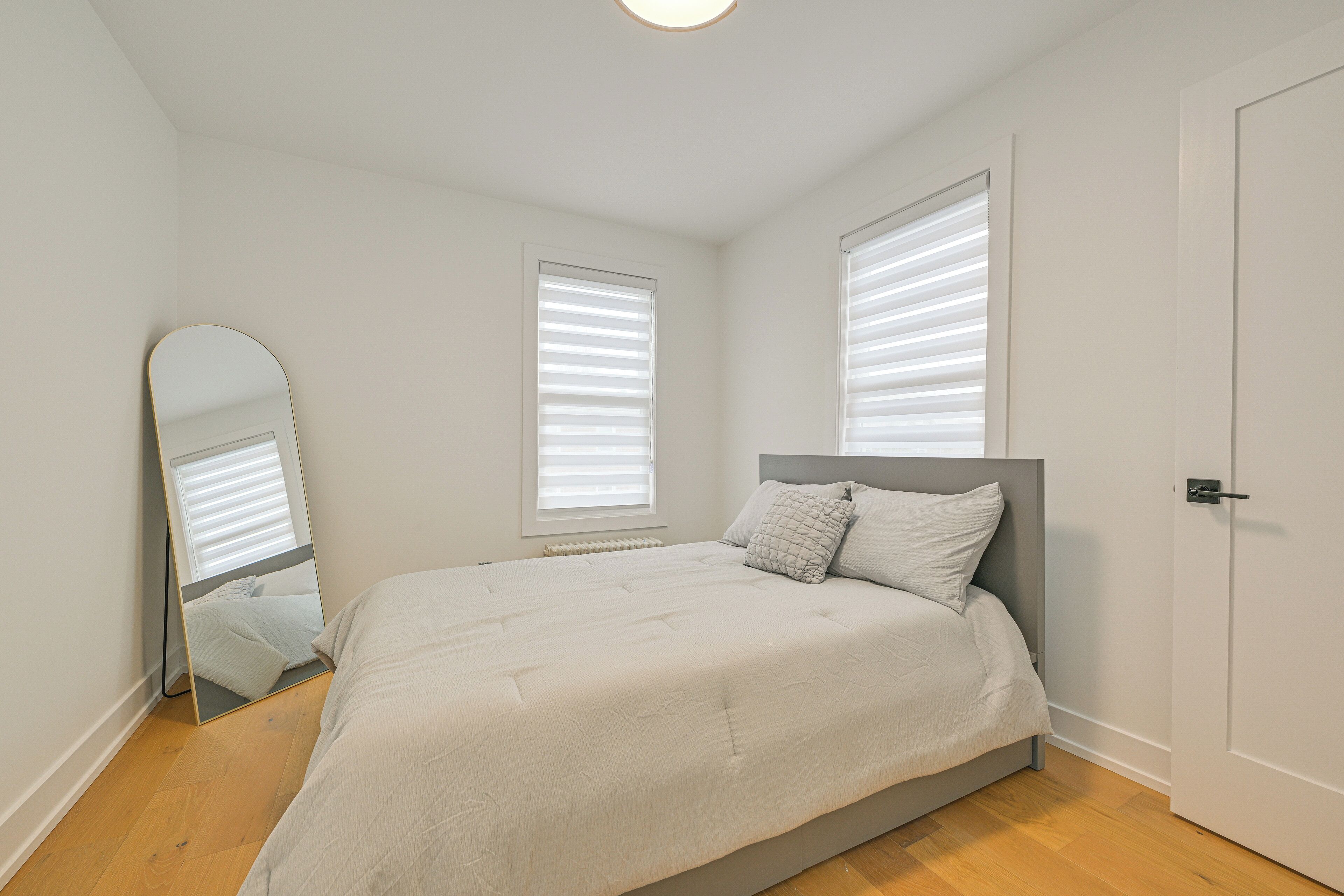 Un dormitorio con cama, un espejo y dos ventanas con persianas.