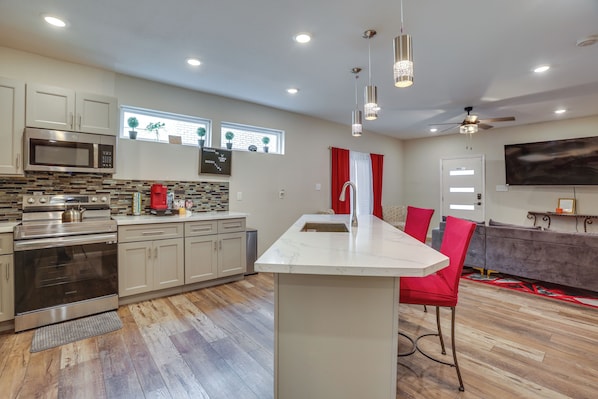 A modern kitchen with a central island, stainless steel appliances, and a dining area with red chairs.