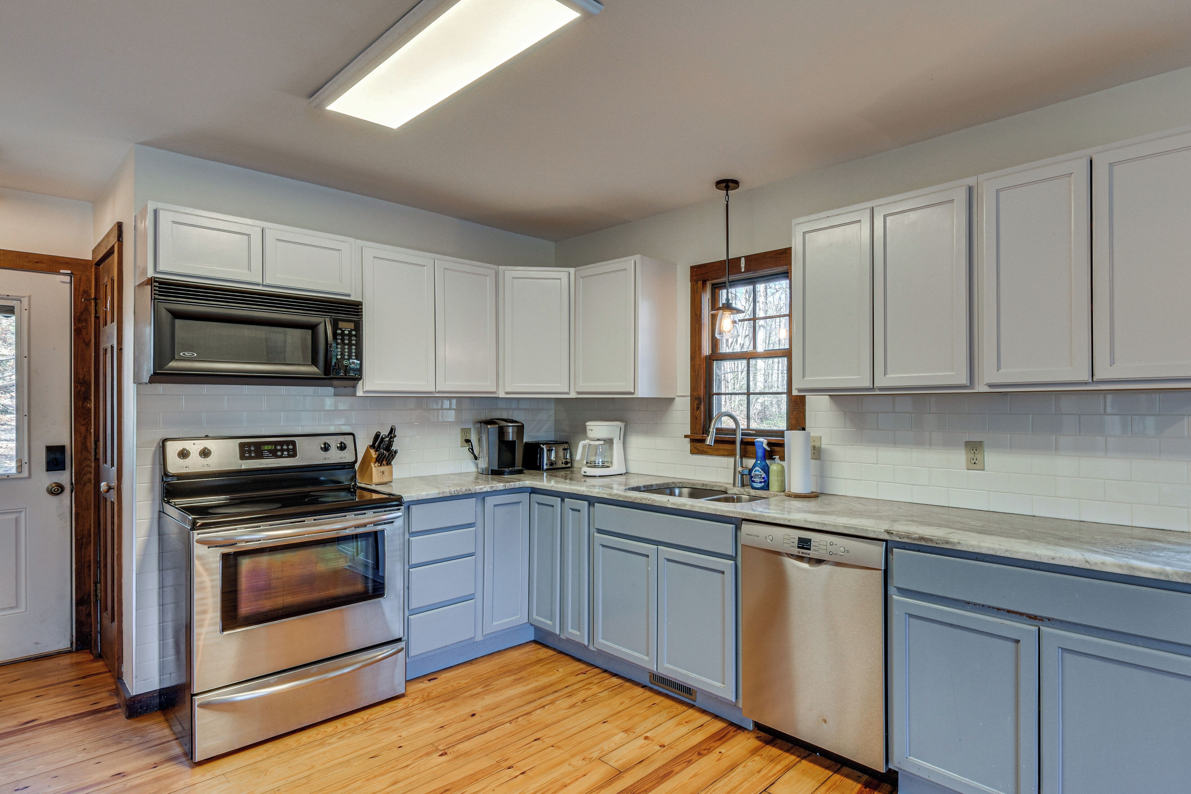 A kitchen with white cabinets, stainless steel appliances, and wooden flooring.