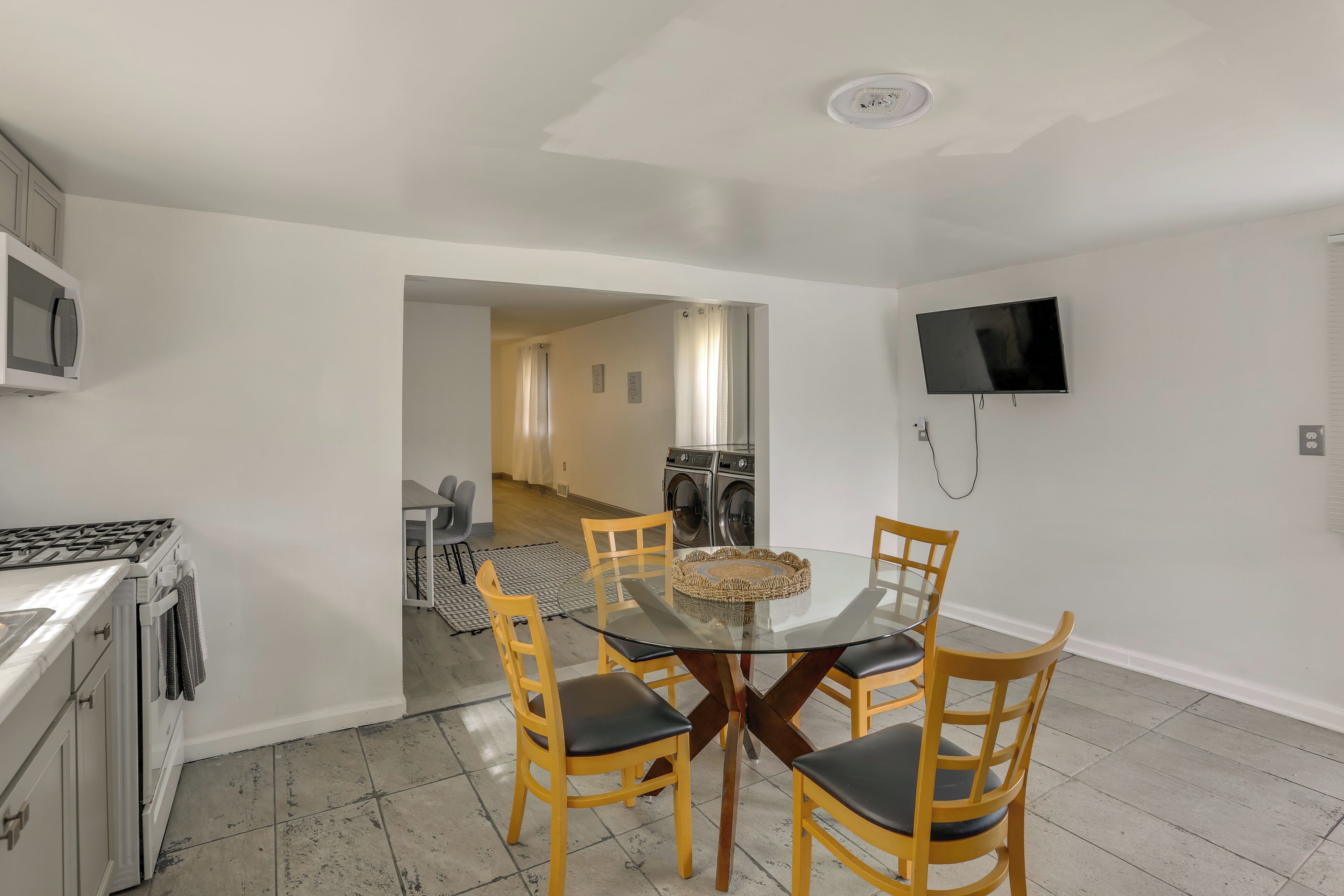A modern kitchen with a gas stove, microwave, and a dining area with a glass table and wooden chairs.