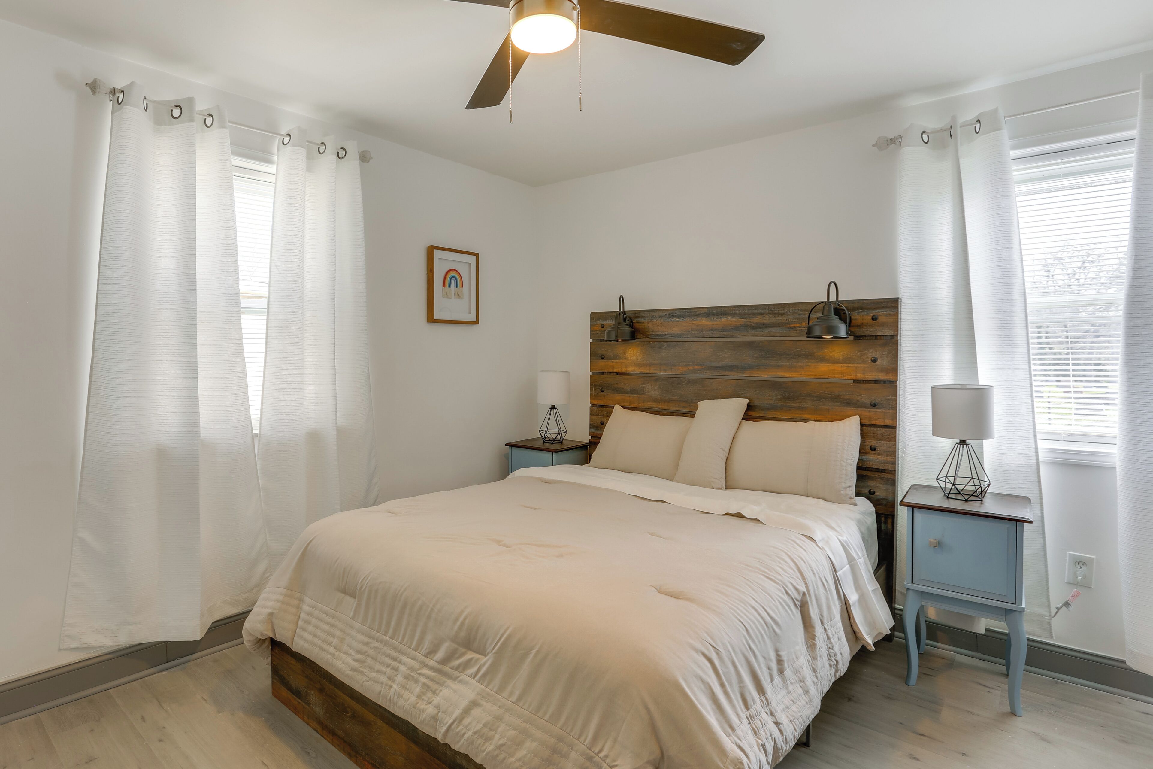 Un dormitorio con cabecera de madera, cama con ropa de cama blanca, mesita de noche con lámpara y ventilador de techo.