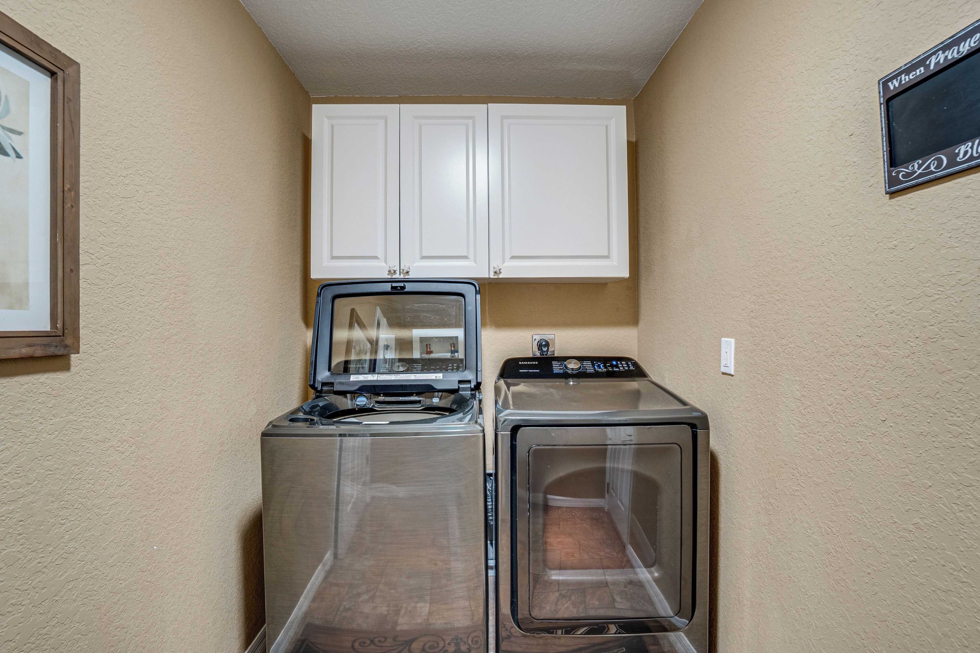 A laundry area with two washers and dryers, white cabinets above, and a sign on the wall.