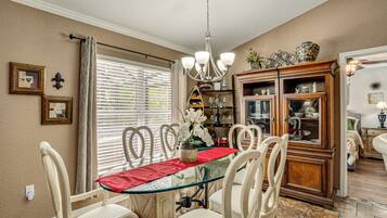 A dining area with a glass table, chairs, a chandelier, and a cabinet with glass doors.