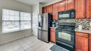 A kitchen with stainless steel appliances, wooden cabinets, a tiled backsplash, and a window with blinds. - Dog-friendly Townhome w/ Patio in Charlotte Area! (Matthews)