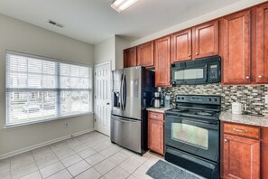 A kitchen with wooden cabinets, stainless steel appliances, a large window with blinds, and a tiled backsplash. - Dog-friendly Townhome w/ Patio in Charlotte Area! (Matthews)