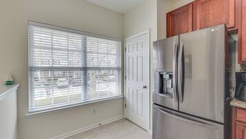 Una cocina con un refrigerador de acero inoxidable, una ventana con persianas y una puerta blanca.