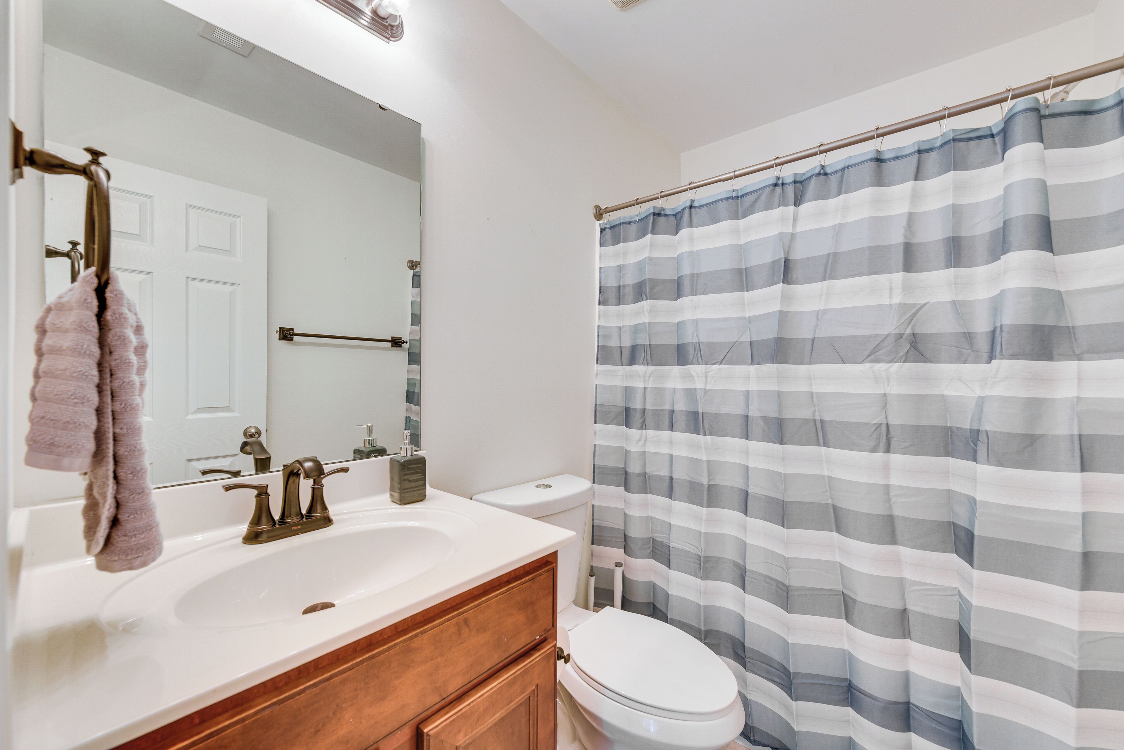 A bathroom with a white sink, a mirror, a towel rack, a toilet, and a striped shower curtain.