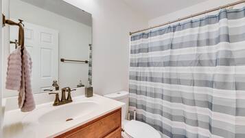 A bathroom with a white sink, a mirror, a towel rack, a toilet, and a striped shower curtain.
