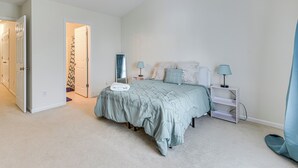 A bedroom with a bed, bedside lamps, a nightstand, a door, and a carpeted floor. - Dog-friendly Townhome w/ Patio in Charlotte Area! (Matthews)